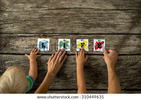 High Angle View of Hands of Family Holding Small Pieces of Colored Paper Together on Top of a Rustic Table For Life Concept.