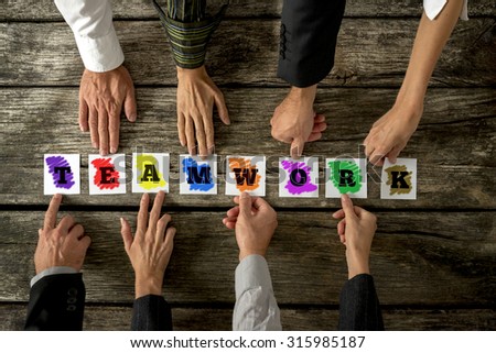 Top view of eight business people assembling the word TEAMWORK while each holding one colorful card with letter on it. Conceptual of cooperation and team building.