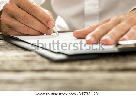 Low angle view of male hand signing contract or subscription form with a pen on a rustic wooden desk.