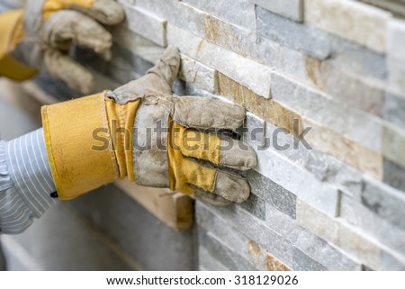 Closeup of manual worker in protection gloves pushing the tile into the cement on the wall while tiling a wall with ornamental tiles l in a DIY, renovation or construction concept.