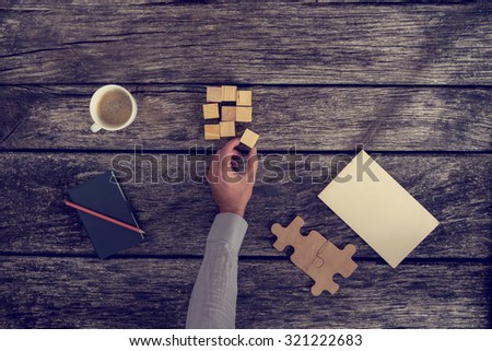 Top View of Businessman Hand Arranging Small Wooden Blocks on Rustic Table with Notes and a Cup of Coffee, Toned Retro Effect.