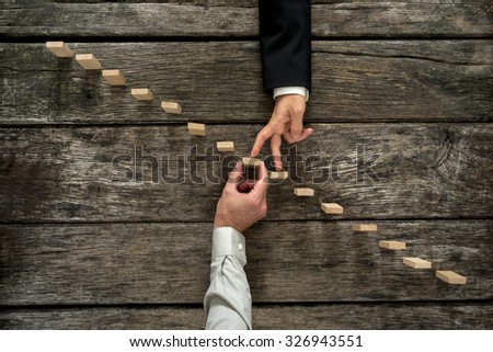 Conceptual image of business partnership and support - businessman supporting wooden step in a staircase made of pegs as his partner walks his fingers up towards growth, achievement and development.