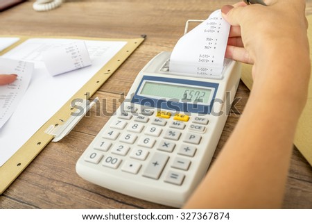 Tax and accounting concept - female accountant calculating costs and expenses using adding machine checking the receipt and comparing it to paperwork and data.