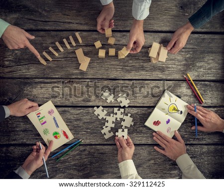 Businesspeople organizing business strategy while holding puzzle pieces, writing down ideas on paper and rearranging wooden blocks. Concept of brainstorming, management, innovation or creativity.