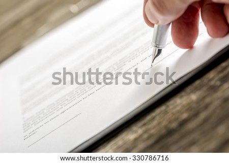 Man signing business document, application, subscription form  or insurance papers with silver pen on wooden desk.
