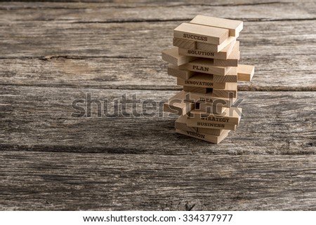 Wooden pegs build in a tower with some of them reading words that represent the most important elements in the way towards success in business - vision, strategy, idea, innovation, plan and solution.