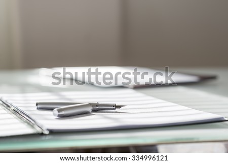 Low angle view of silver ink pen lying on white sheet of paper in a folder with another set of paperwork at the opposite side of the desk.