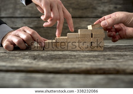 Team effort on the way to success - two male hands building stable steps with wooden pegs for the third one to walk his fingers up towards personal and career growth.