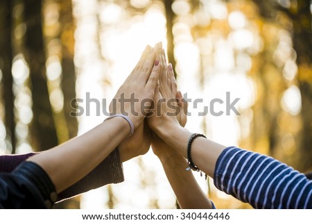 Closeup view of four people joining their hands together high up in the air outside in a forested area.