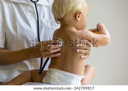 Closeup of female pediatric medical doctor using a stethoscope to listen to lungs of a baby as he or she sits wearing just a diaper in her lap.