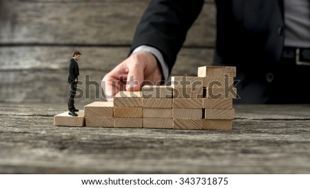Businessman building a staircase of wooden pegs for another entrepreneur to climb up the ladder of success.
