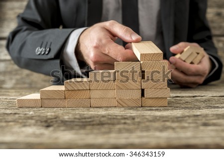 Front closeup view of businessman constructing steps of wooden pegs with focus to the peg in his hand, shallow dof.