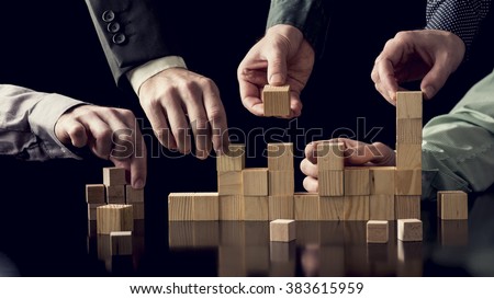 Teamwork and cooperation concept - five male hands building a structure of wooden blocks on black desk with reflection, toned retro effect.