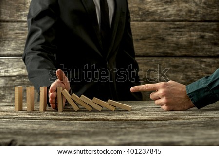 Businessman pointing to falling dominos and his partner stopping them in a conceptual image of cooperation and mentor.