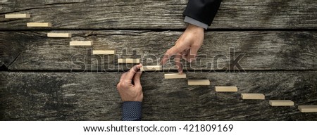 Hand of a businessman supporting a wooden step for his colleague to walk his fingers up towards success, conceptual of business teamwork and collaboration.