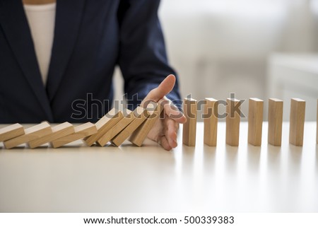 Close up view on hand of business woman stopping falling blocks on table for concept about taking responsibility.