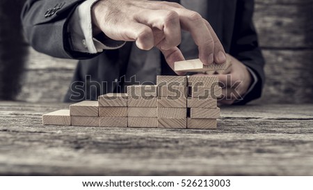 Businessman building a graph or ladder of success on old rustic wooden table.