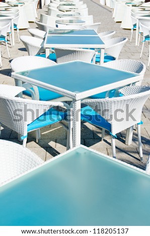 Rows of empty tables and white wicker chairs in an open air cafeteria. Cafe bar on sunny summer day.