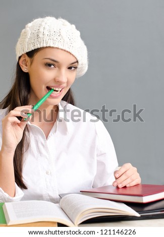 Beautiful brunette student girl holding a pen. Dressed in white wearing a beret. Learning can be sexy!