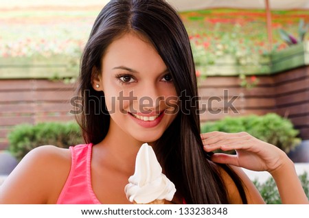 Beautiful woman smiling and holding an ice cream. Girl relaxing at a terrace on a hot day with a delicious ice cream.