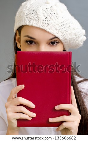 Piercing eyes looking over a notebook. Beautiful student girl holding a notebook. Dressed in white wearing a beret.