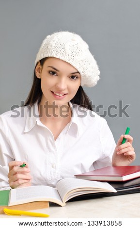 Beautiful brunette student girl holding a pen. Dressed in white wearing a beret.