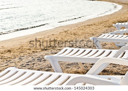 Row of white plastic deck chairs on the beach in the morning.