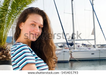 Summer marine scene with a beautiful girl. Attractive girl wearing a blouse with stripes at the sea side. Yachts in the background.