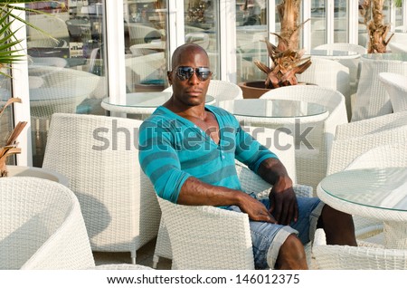 Black man sitting at a bar. Handsome fit man sitting alone a street terrace. Summer outdoors.