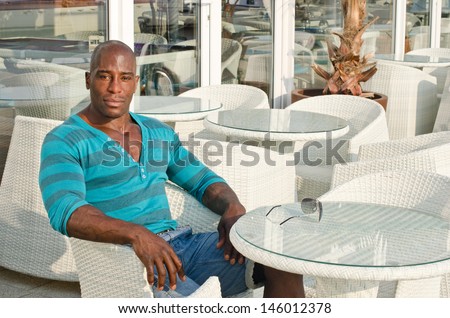 Black man sitting at a bar. Handsome fit man sitting alone a street terrace. Summer outdoors.