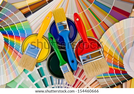 Paint cans and brushes on stripes of color swatches. Sample of colorful paint. Cans of red, yellow, blue and green paint.