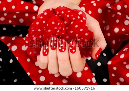 Close up on beautiful female hand with cute red manicure with white dots. Black and red dotted background.