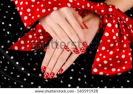 Close up on beautiful female hands with cute red manicure with white dots. Black dotted background.