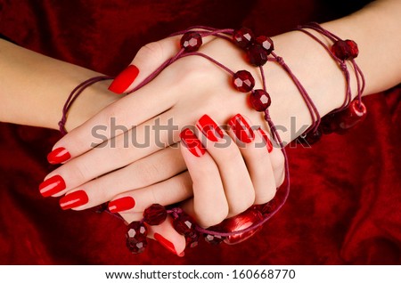 Close up on beautiful female hands with sexy red manicure. Red velvet background.