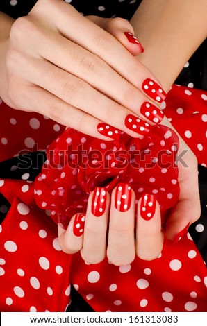Close up on beautiful female hands with cute red manicure with white dots. Black and red dotted background.