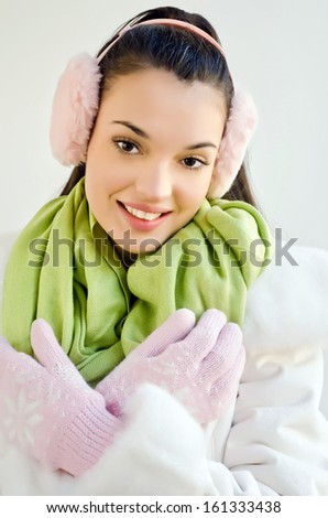 Beautiful young woman dressed for winter season. Girl wearing pink gloves and ear muffs and a green scarf.