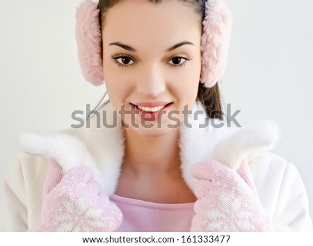 Beautiful girl smiling wearing pink ear muffs and cute gloves with snowflake. Woman dressed for winter season.