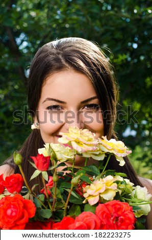 Beautiful woman in the garden smelling flowers. Girl smelling a bouquet of red and yellow roses on a hot summer day.