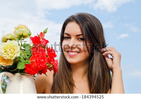Beautiful woman in the garden with flowers. Girl smiling near a vase of red and yellow roses on a hot summer day.