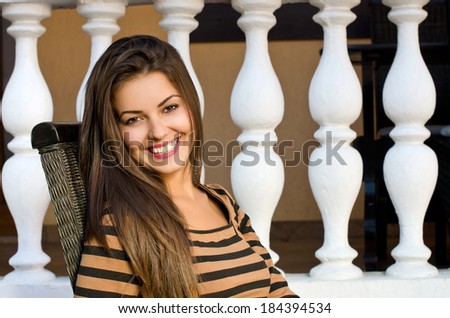 Beautiful girl smiling sitting on a chair.  Woman sitting outside, background nice architecture with columns.