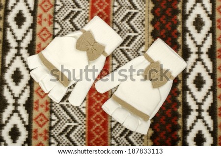 Cute white mittens. A pair of white gloves with a brown bow on pattern winter scarf background.