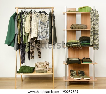 Dressing closet with military camouflage khaki green clothes arranged on hangers and shelf.  Wardrobe with camo pattern clothes, shoes and accessories.