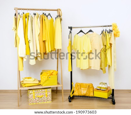 Dressing closet with yellow clothes arranged on hangers. Wardrobe full of all shades of yellow clothes, shoes and accessories.