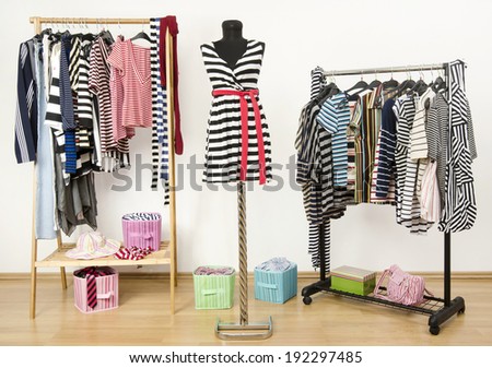 Dressing closet with striped clothes arranged on hangers and a  black and white outfit on a mannequin.  Colorful wardrobe full of clothes and accessories with stripes pattern.