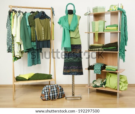 Dressing closet with green clothes arranged on hangers and shelf, autumn outfit on a mannequin. Wardrobe full of all shades of green clothes and accessories.