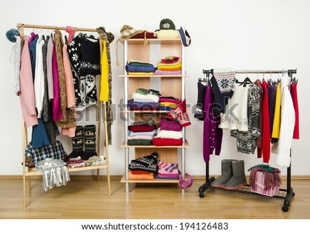 Wardrobe with winter clothes nicely arranged. Dressing closet with colorful clothes and accessories on hangers and a shelf.