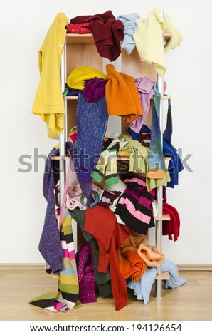 Messy winter clothes thrown on a shelf. Untidy cluttered wardrobe with colorful clothes and accessories.