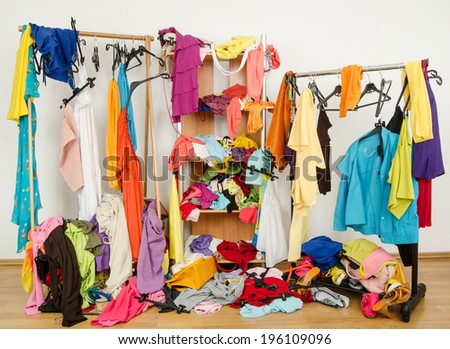 Untidy cluttered woman wardrobe with colorful clothes and accessories. Messy clothes thrown on a shelf, on the ground and off the hangers and racks.