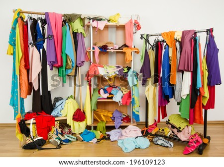 Untidy cluttered woman wardrobe with colorful clothes and accessories. Messy clothes thrown on a shelf, on the ground and off the hangers and racks.