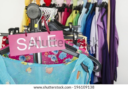 Close up on a big sale sign for summer clothes. Clearance rack with colorful summer outfits and accessories displayed on hangers.
